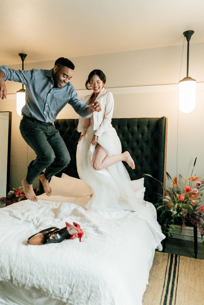 Desmond and Chanel jumping on bed at Hotel G wearing ethically-made Kali Made Garments menswear, Ermis Nava shoes, Celia Grace wedding dress, Brevity Brand jacket, Soko jewelry, and vintage accessories