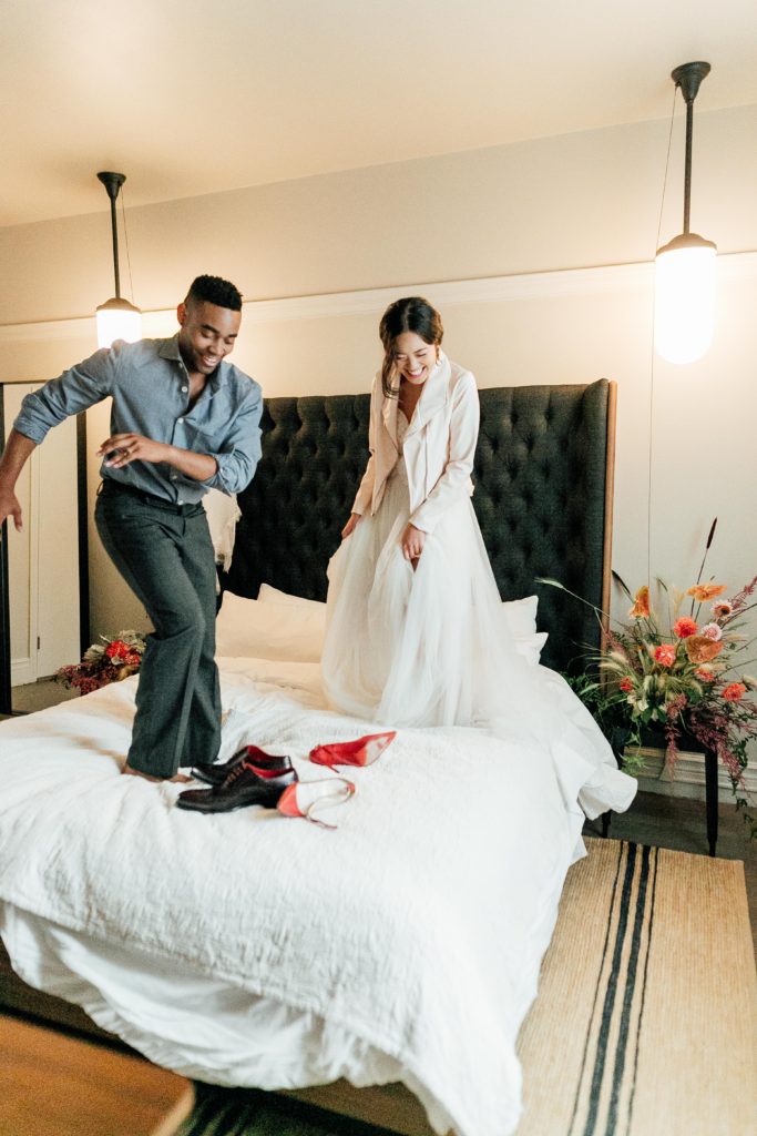 Desmond and Chanel jumping on bed at Hotel G wearing ethically-made Kali Made Garments menswear, Ermis Nava shoes, Celia Grace wedding dress, Brevity Brand jacket, Soko jewelry, and vintage accessories