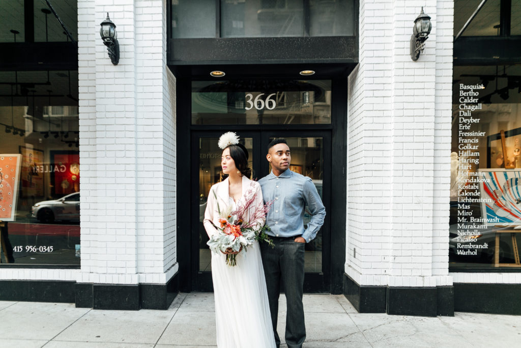 Desmond and Chanel in downtown San Francisco wearing ethically-made Kali Made Garments menswear, Ermis Nava shoes, Celia Grace wedding dress, Brevity Brand jacket, Soko jewelry, and vintage accessories showcasing Claire Xue florals