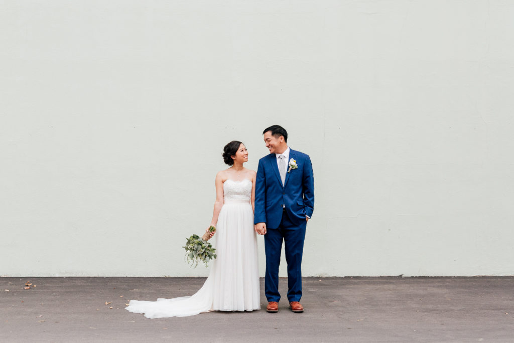 bride and groom look into each other's eyes against grey wall