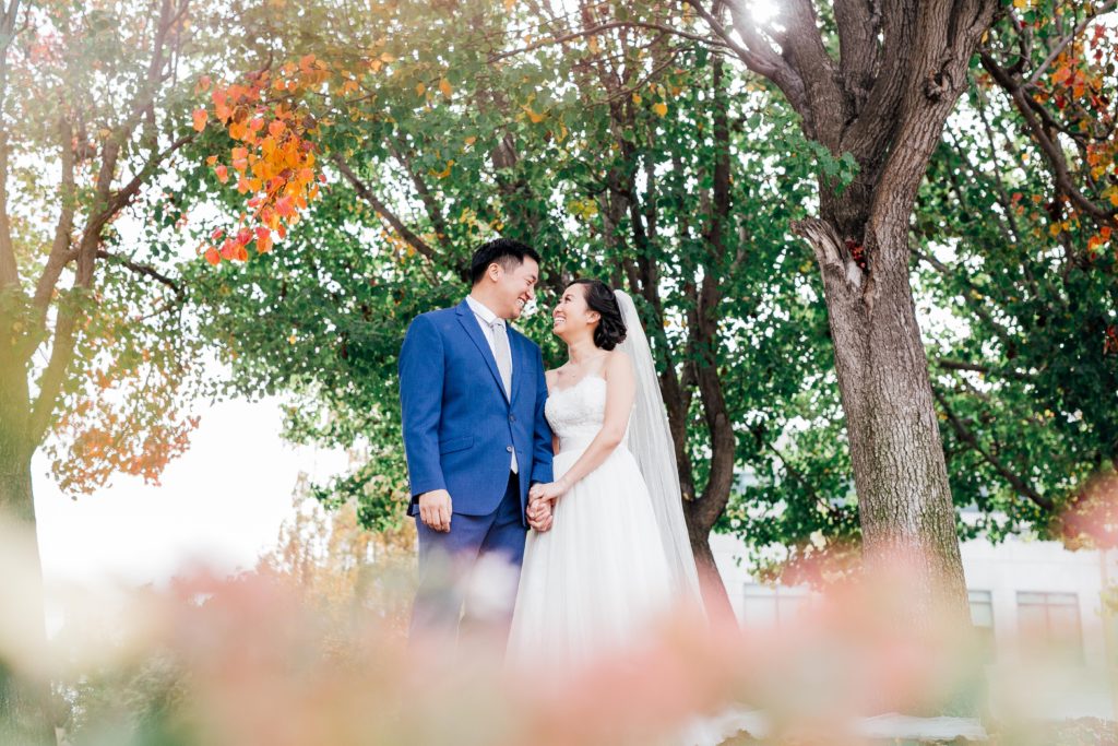 bride and groom stare into each other's eyes amidst fall trees 