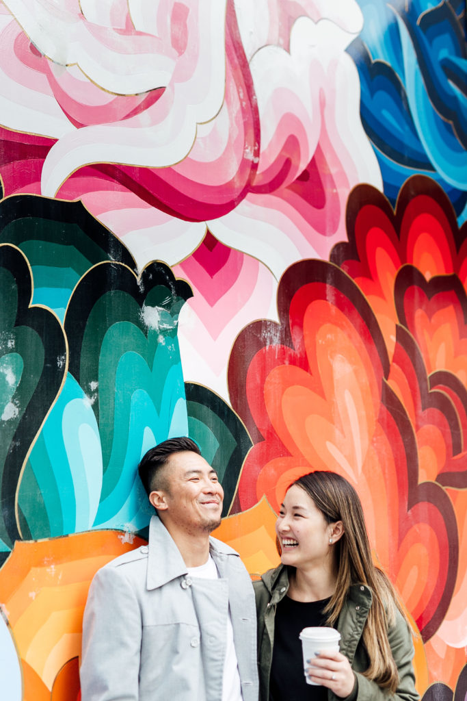 couple stands together in front of a colorful mural