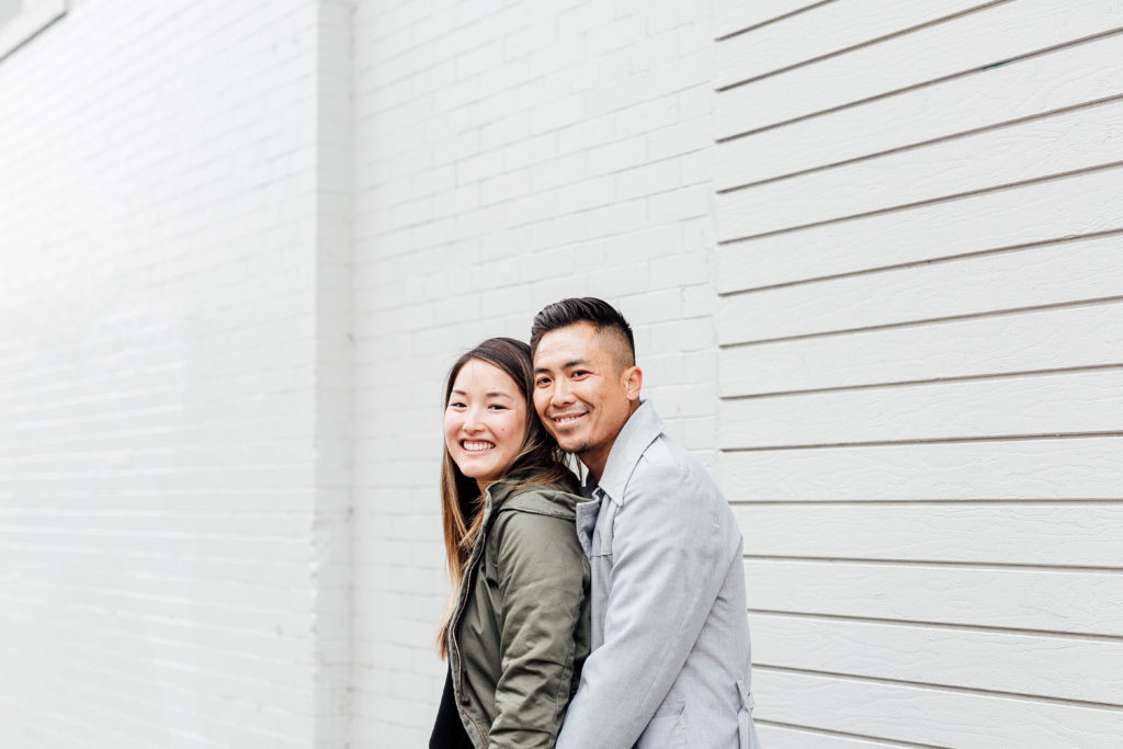 engaged couple pose in front of white wall