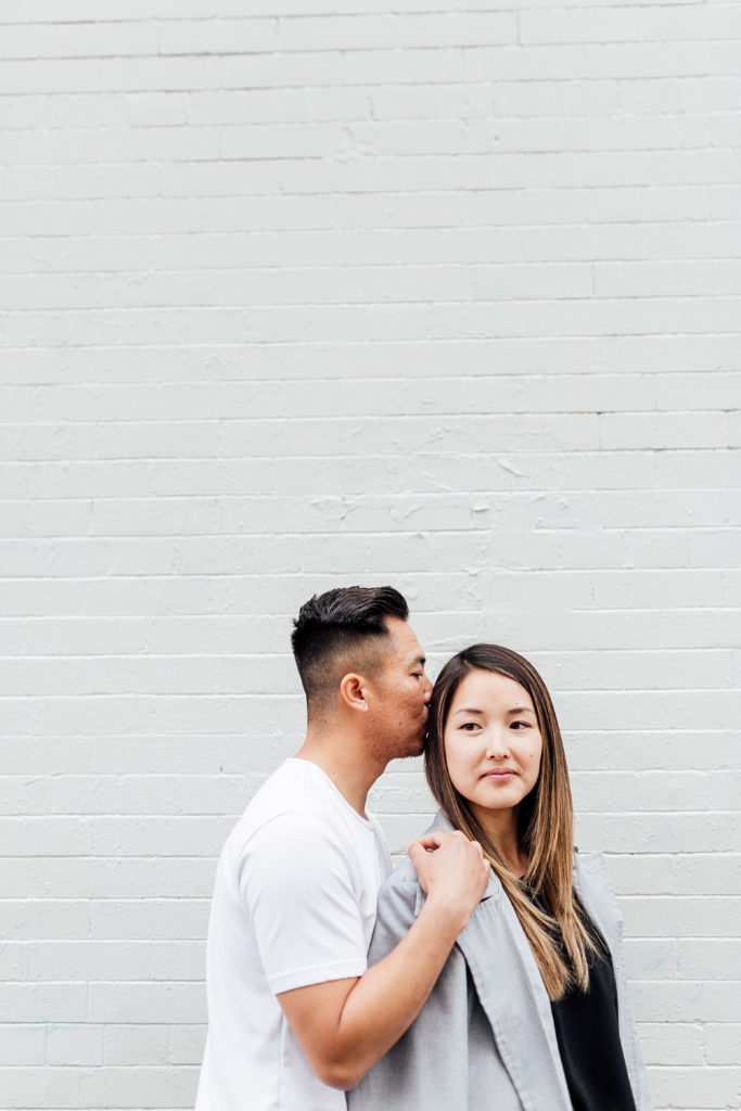 couple poses in front of blank wall, fiancée looks into distance