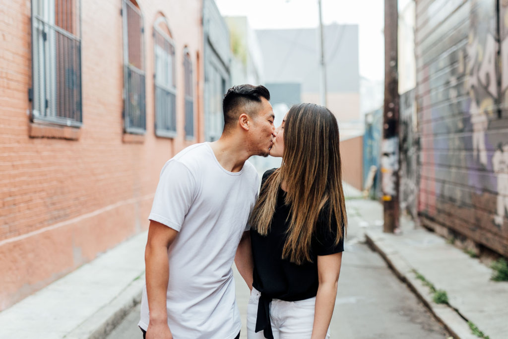 couple kisses while standing in the middle of an alley