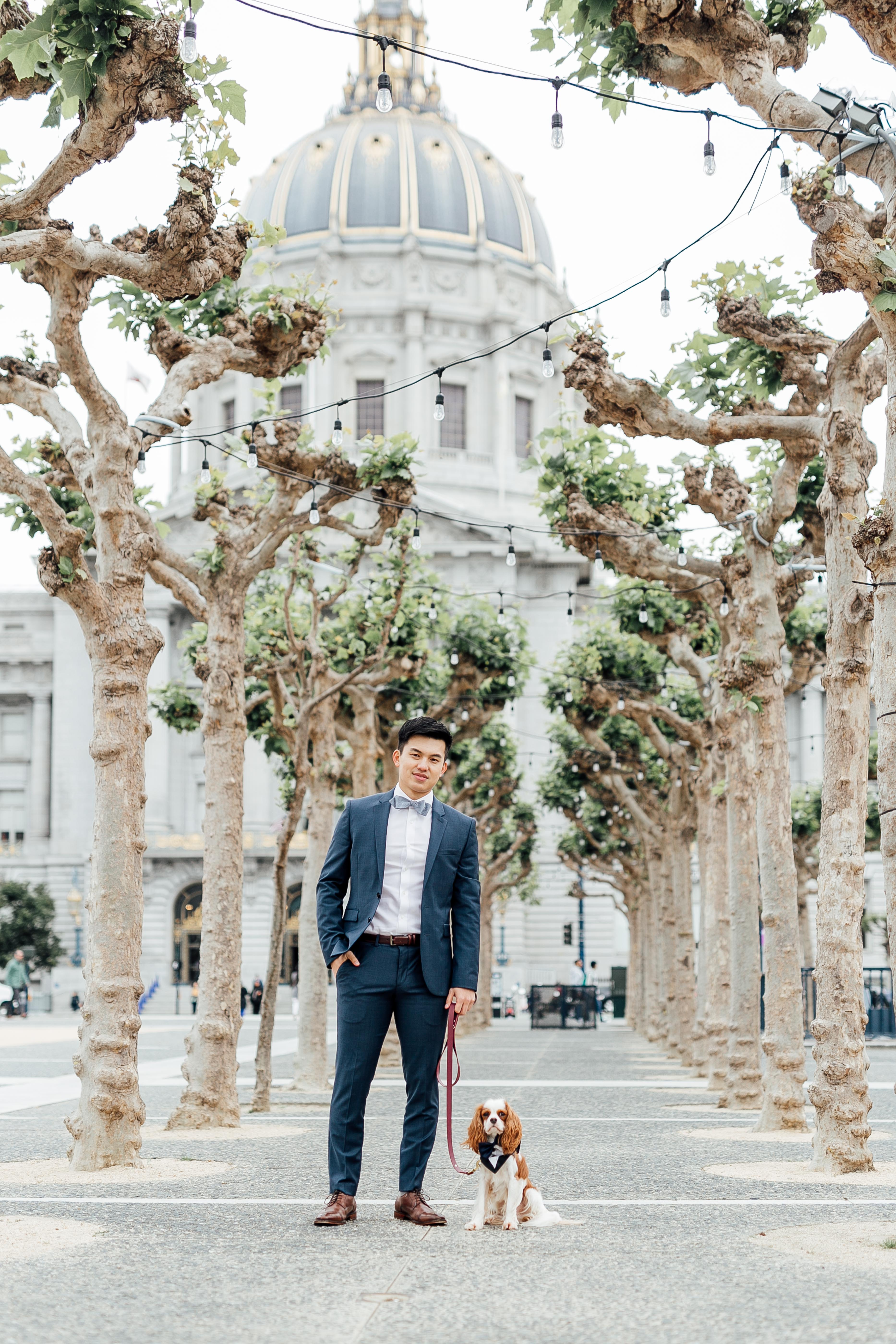 Groom stands posed with dog outside of City Hall