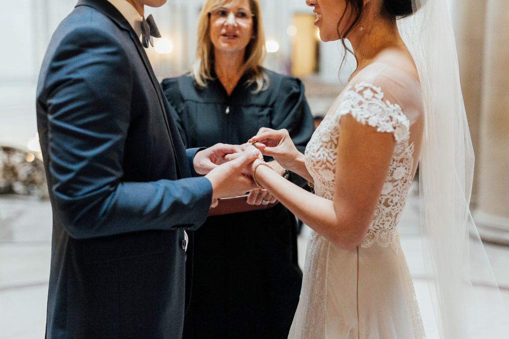 Detail shot of bride and groom holding hands in front of wedding officiant