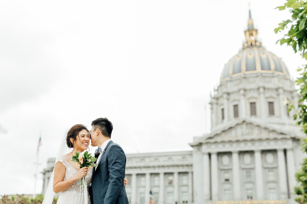 Bride and groom embrace in front of grand City Hall building