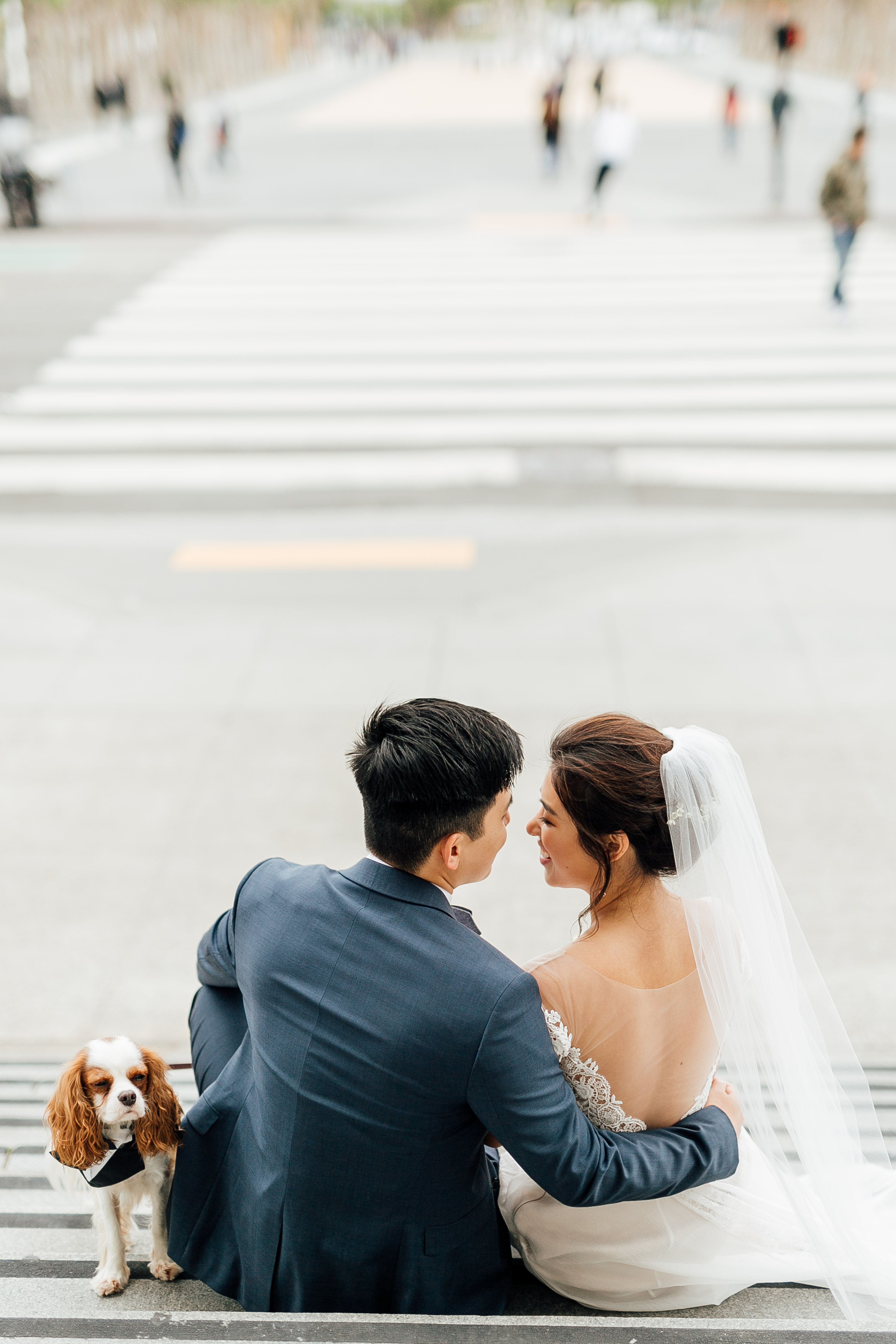 Bride and groom lean in for kiss on steps, dog looks at camera