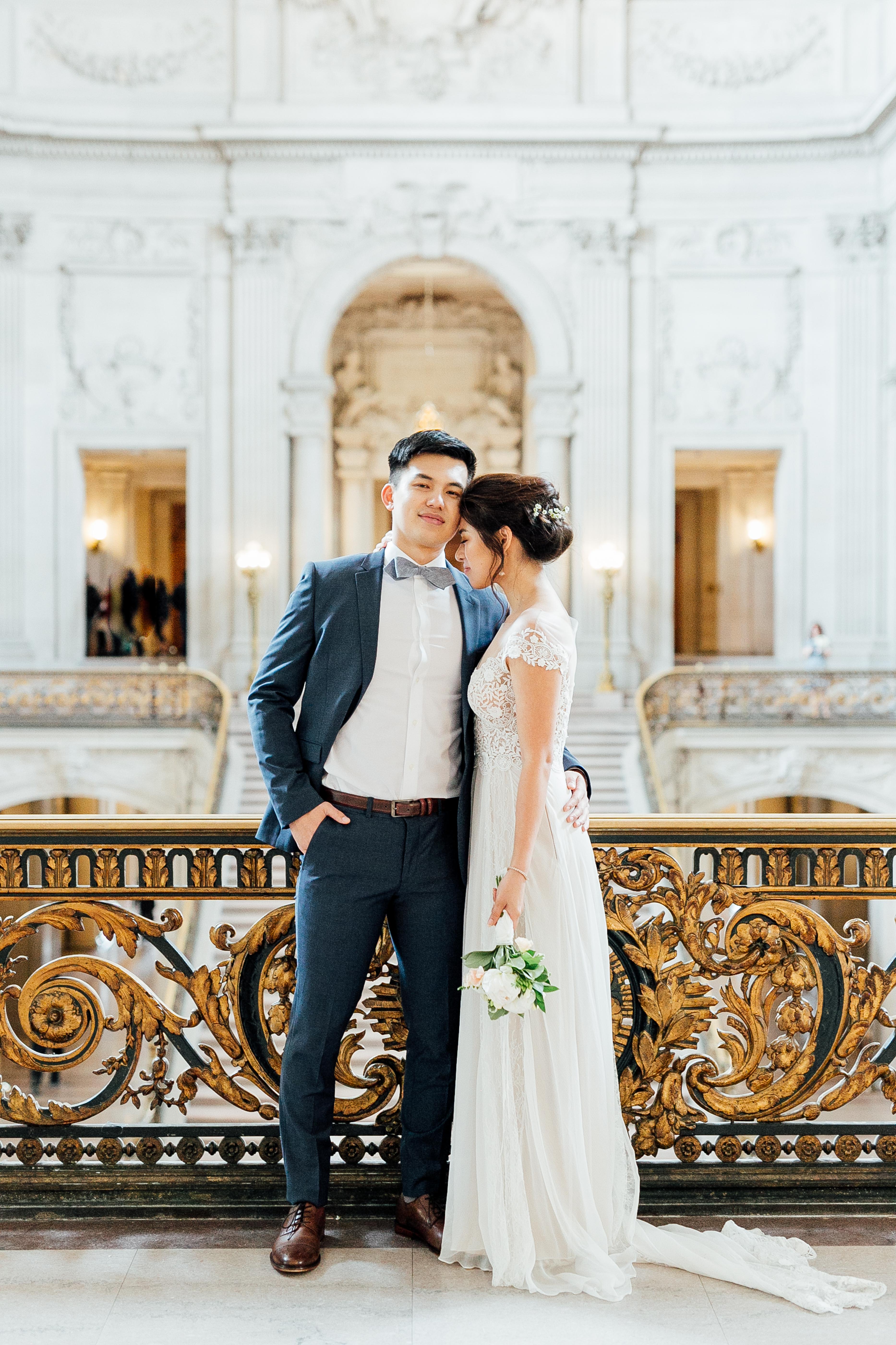 Bride and groom stand on balcony in front of elegant City Hall interior