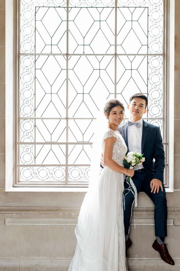 Bride and groom smile during photoshoot at 3rd floor windows inside San Francisco City Hall