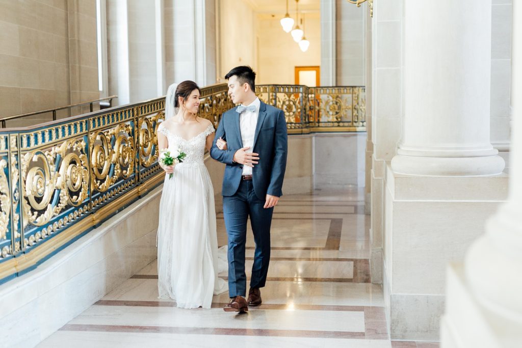 Bride and groom smile during photoshoot at 3rd floor railings inside San Francisco City Hall