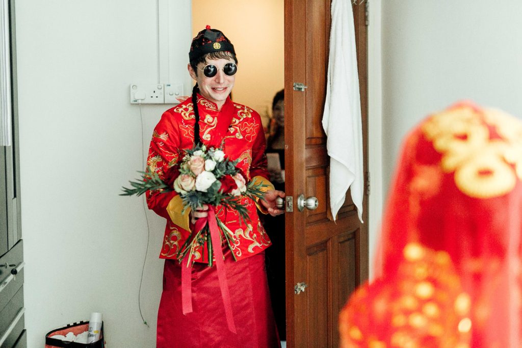 Groom walking through door in traditional garb and with bouquet