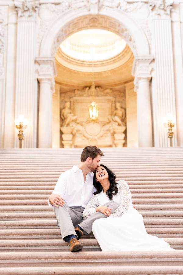 The bride and groom sit on the stairs of their San Francisco city hall wedding
