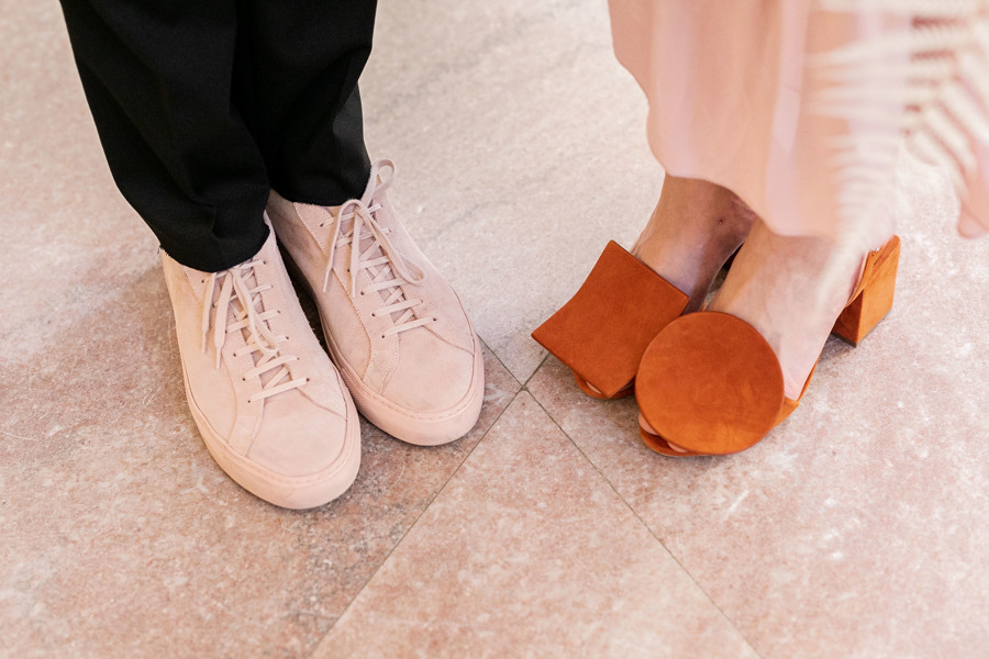 A picture of Mickael and Claire's unique shoes at their wedding at San Francisco City Hall. Michael wears blush colored tennis shoes and Claire wears rust colored heels featuring large shapes.