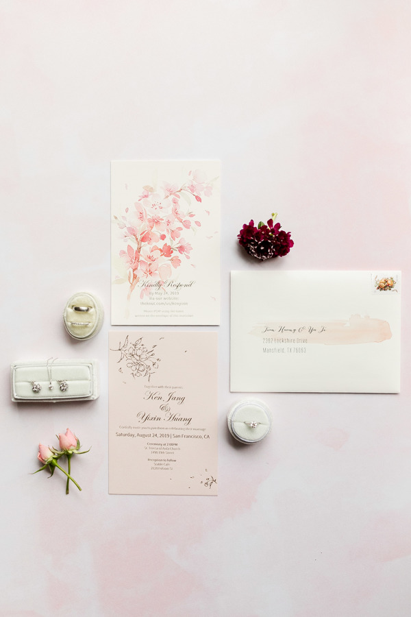 Wedding invitations in a flat lay with the bride's jewelry and flowers.